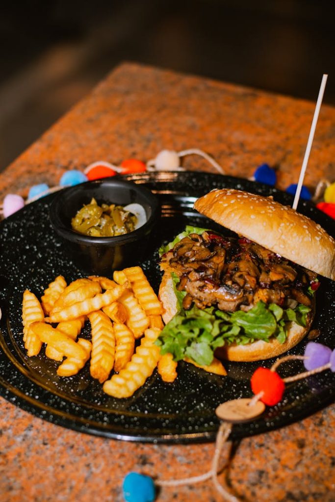 A mouthwatering gourmet burger with crinkle fries and relish on a black ceramic plate.